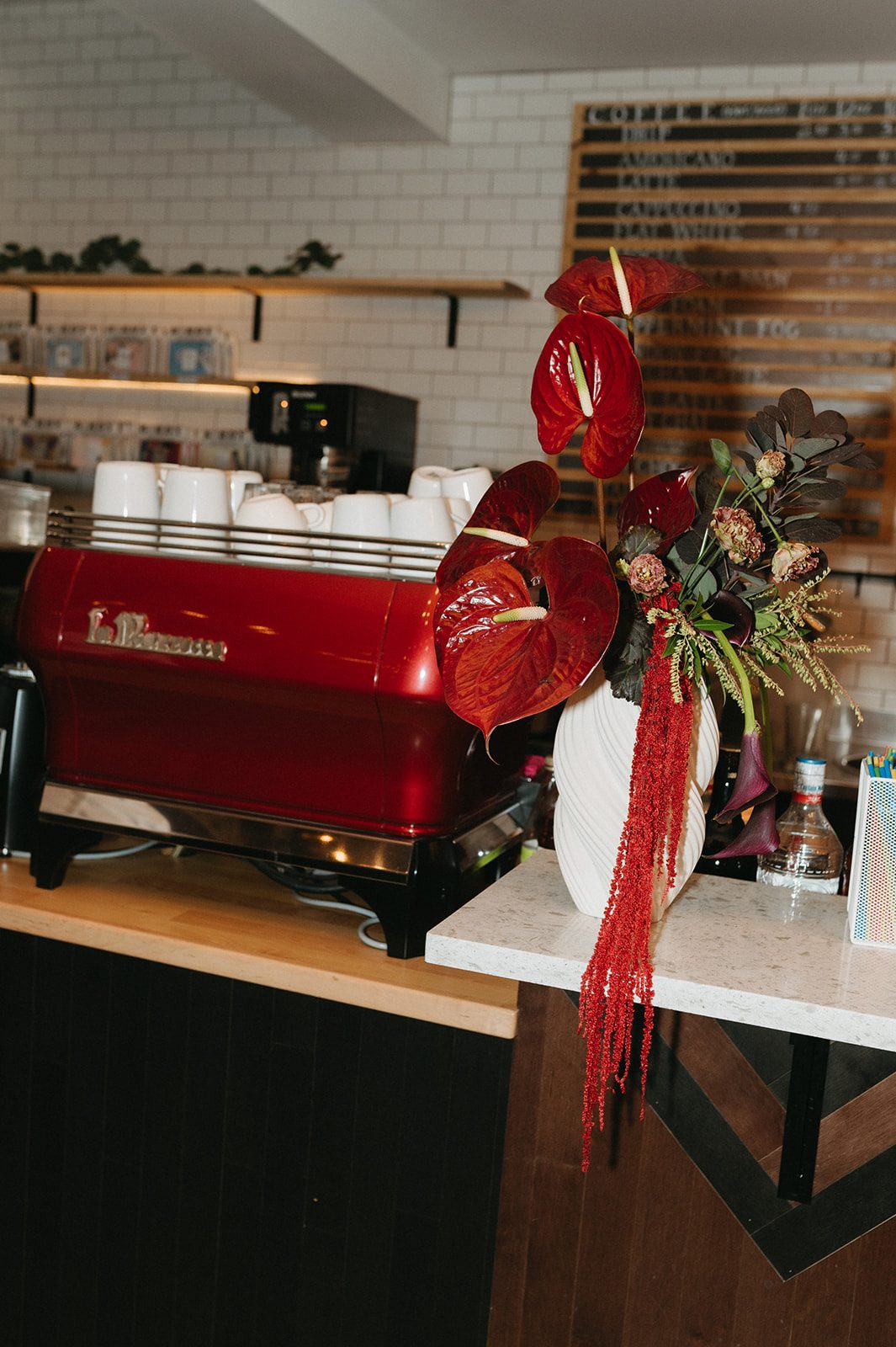 Andi + Logan Burgundy sculptural wedding flowers displayed beside a red espresso machine at a modern fall wedding reception.