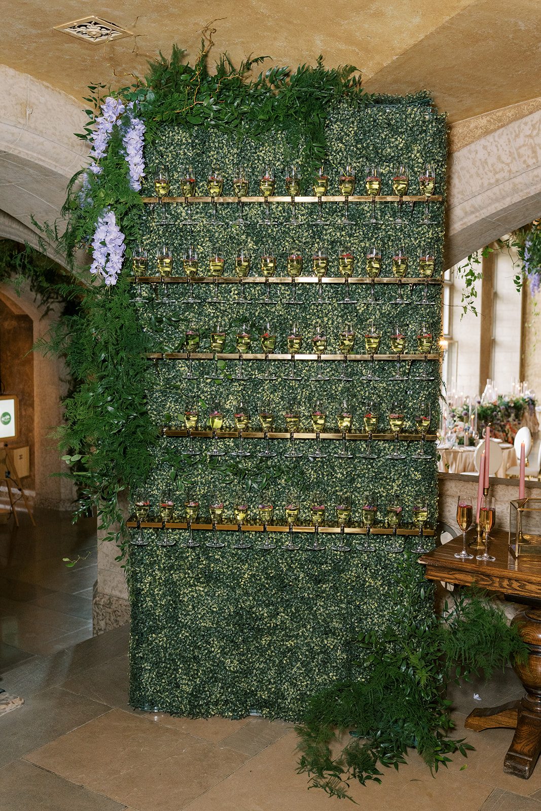 Lottie Green champagne wall framed with lush greenery and cascading lavender flowers at Fairmont Banff Springs Wedding.
