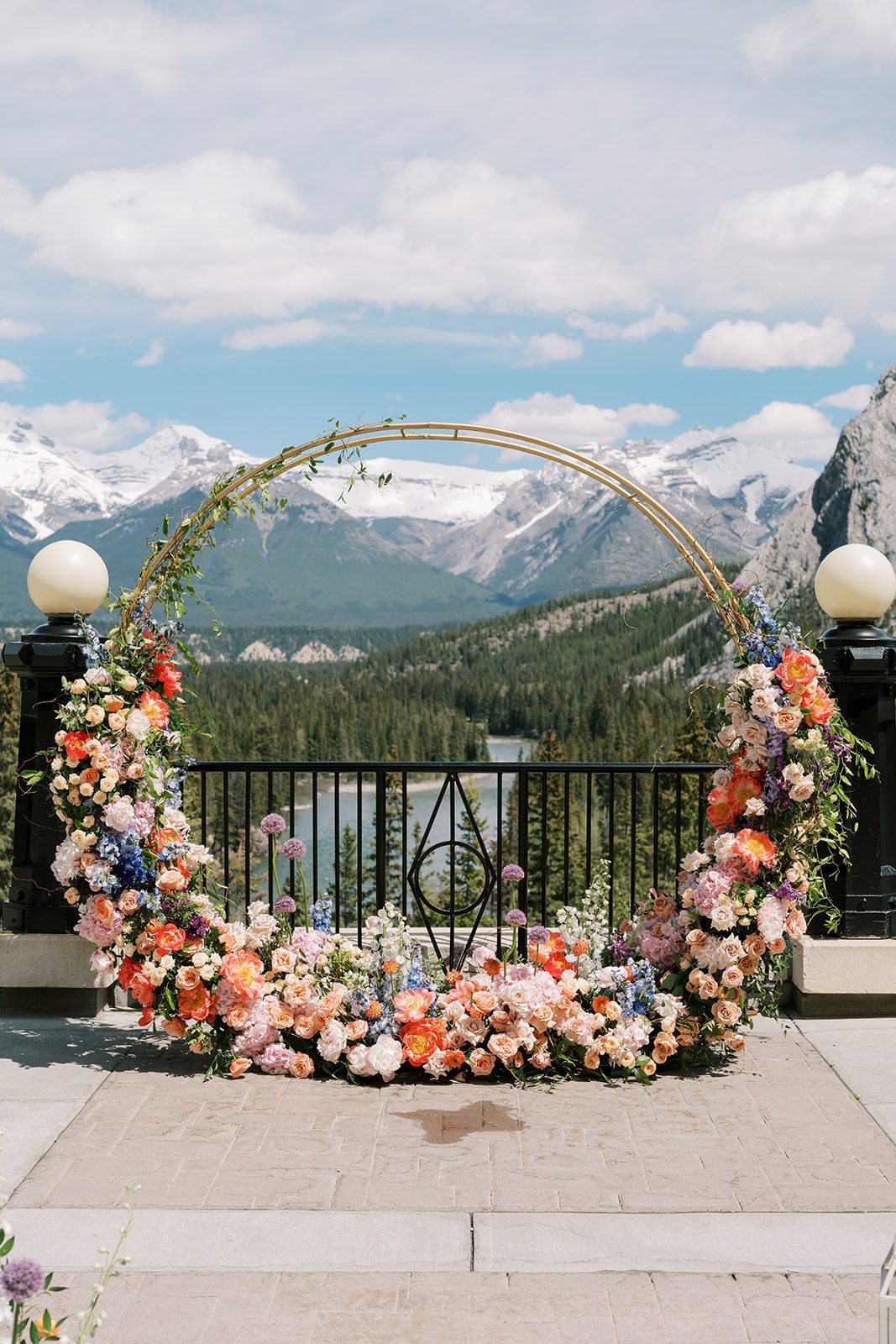 Lottie Fairmont Banff Springs wedding ceremony arch filled with colourful garden flowers against a panoramic Rocky Mountain backdrop.