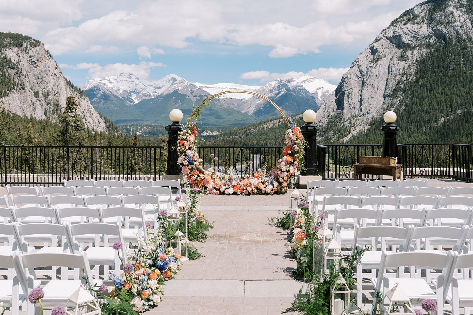 Lottie Fairmont Banff Springs wedding ceremony on the outdoor terrace with colourful floral arch, aisle flowers and Rocky Mountain views.