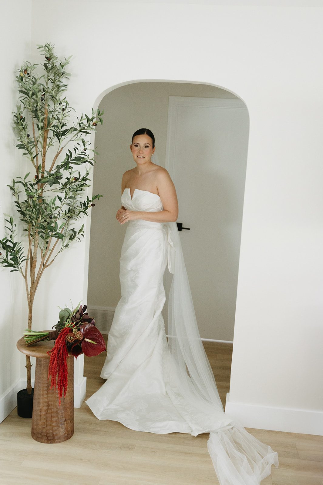 Andi + Logan Fall bride beside her sculptural wedding flowers featuring burgundy anthurium and cascading red amaranthus.