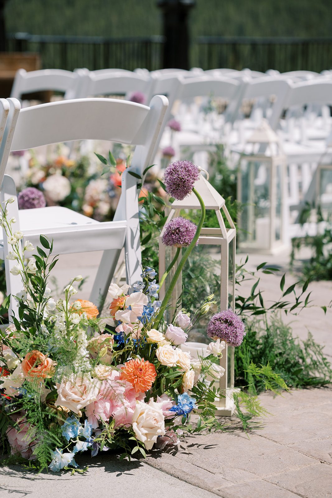 Lottie Garden inspired wedding aisle flowers with purple allium, coral blooms, blue delphinium and white lanterns.