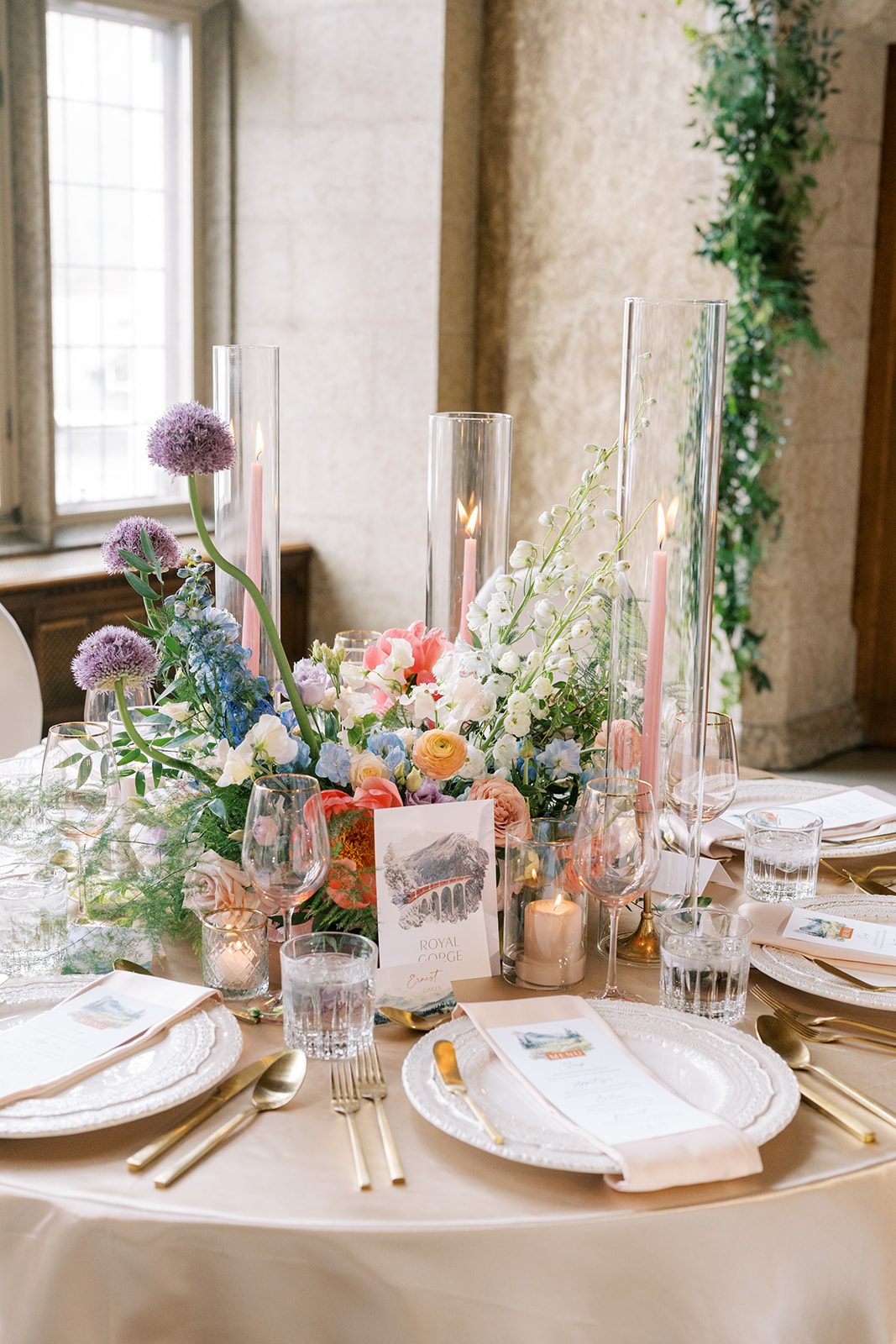 Lottie Colourful garden inspired wedding centrepiece with coral, peach, blue, lavender and white flowers surrounded by candlelight.