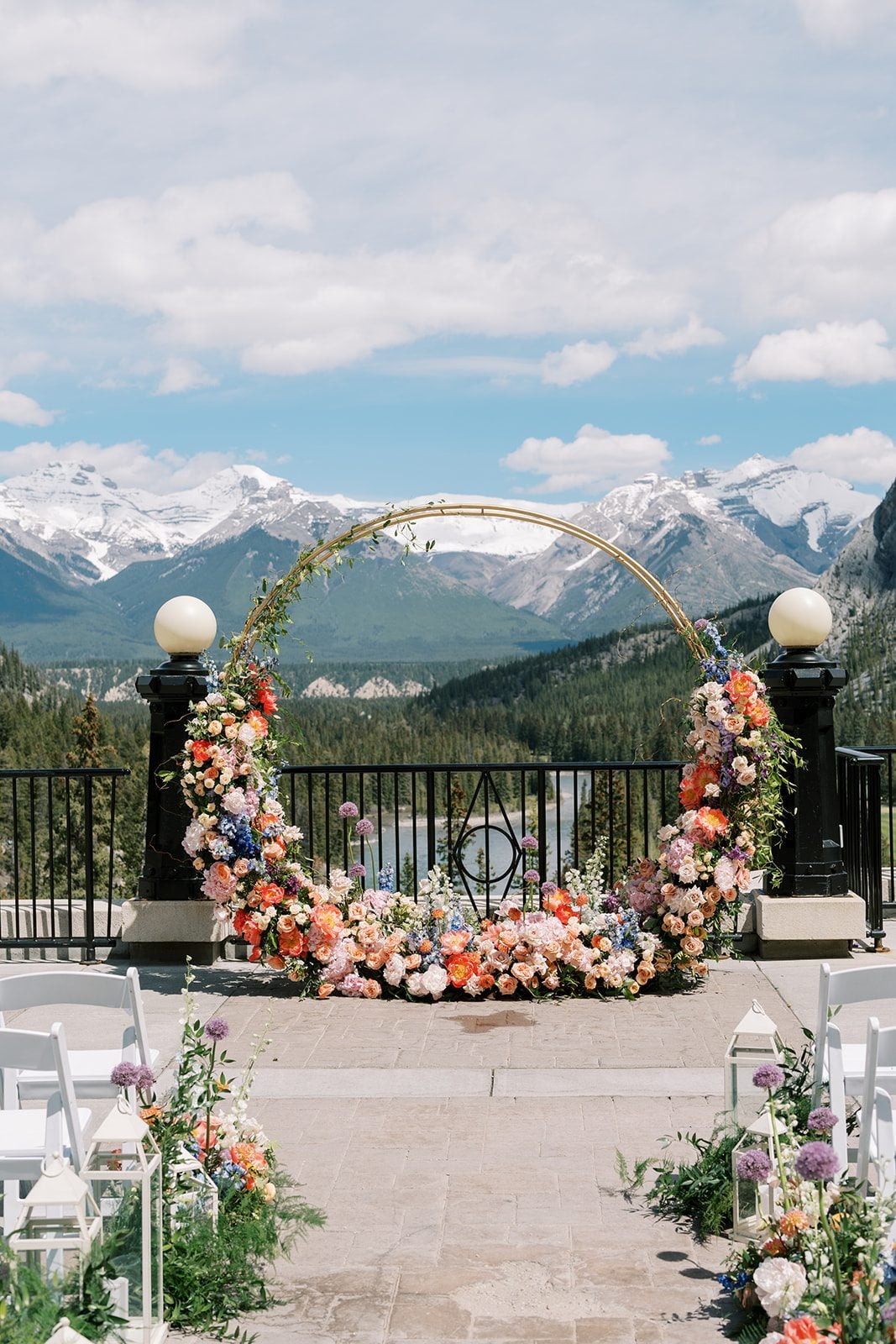 Lottie Colourful circular floral arch framing the Rocky Mountains at a Fairmont Banff Springs wedding ceremony.