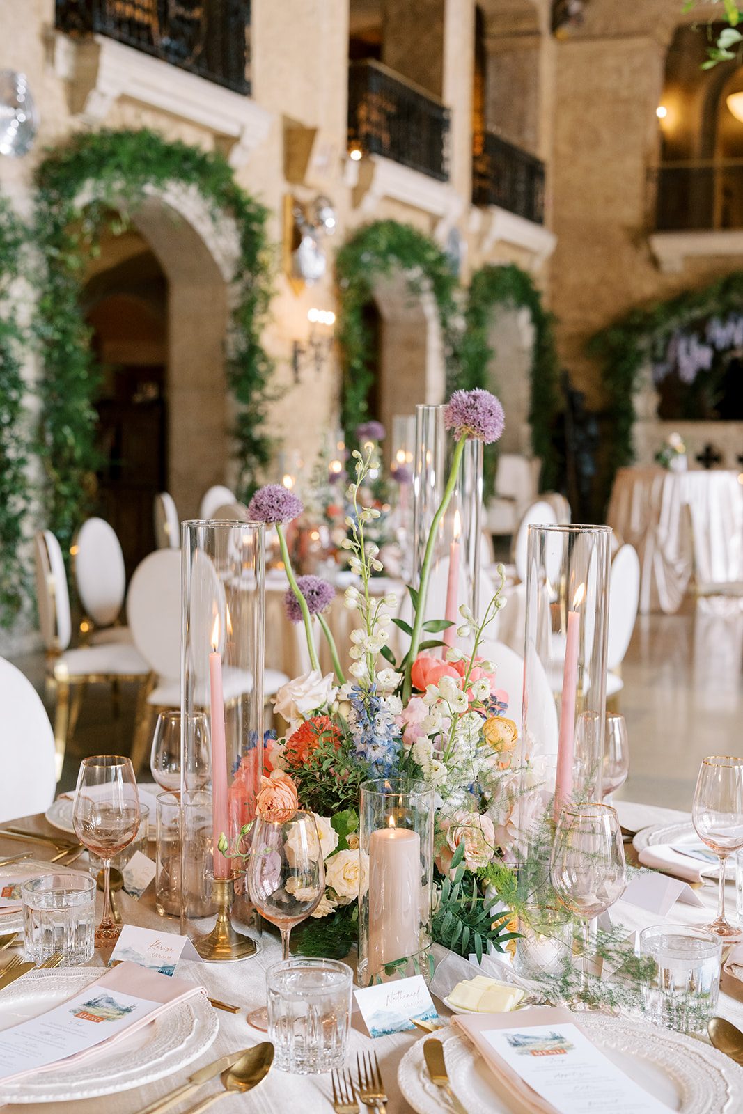 Lottie Garden inspired wedding centrepiece with coral peonies, peach ranunculus, blue delphinium, white flowers and sculptural purple allium.