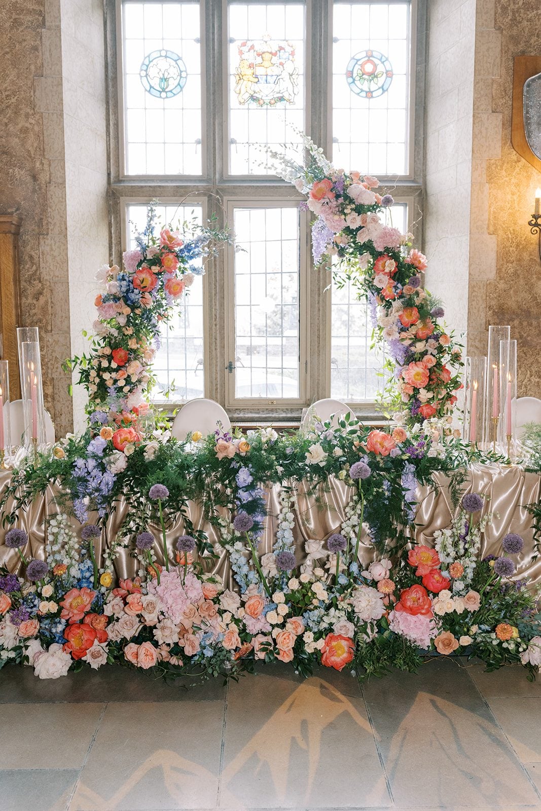 Lottie Lush garden inspired head table flowers with coral peonies, blush roses, blue delphinium, purple allium and cascading greenery.
