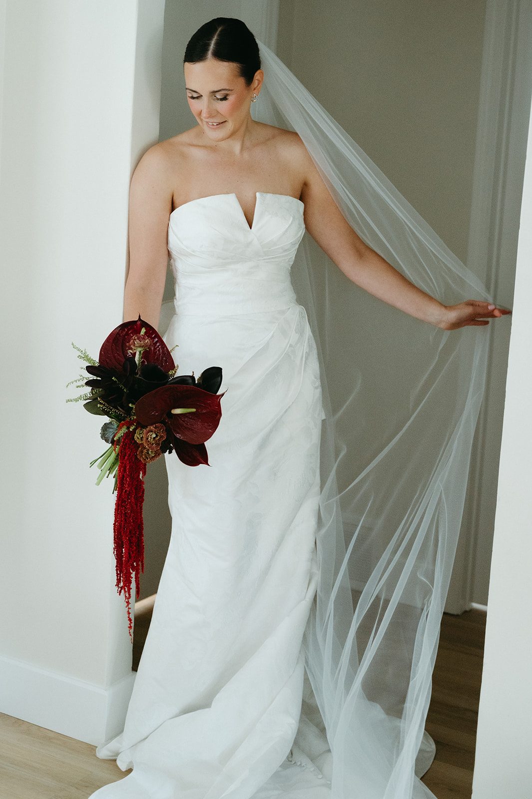 Andi + Logan Bride holding a rich toned sculptural wedding bouquet with burgundy anthurium and cascading red amaranthus.