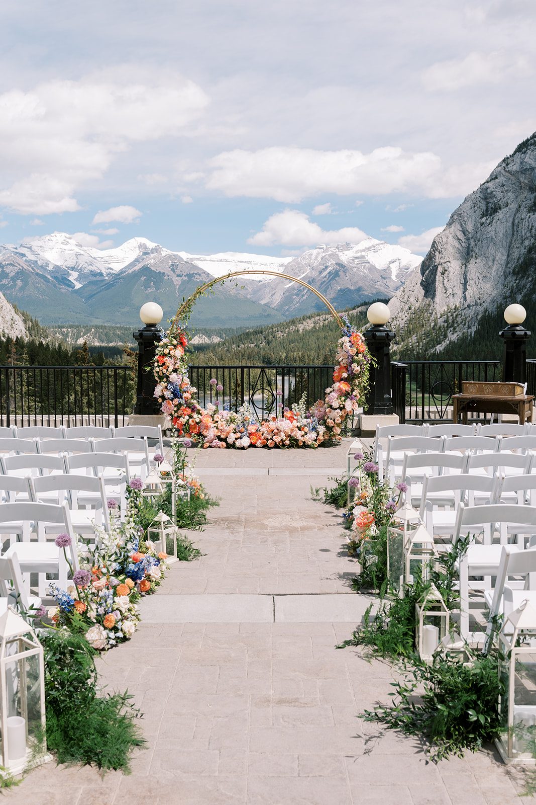 Lottie Fairmont Banff Springs wedding on the outdoor terrace with colourful aisle flowers, circular floral arch and mountain views.