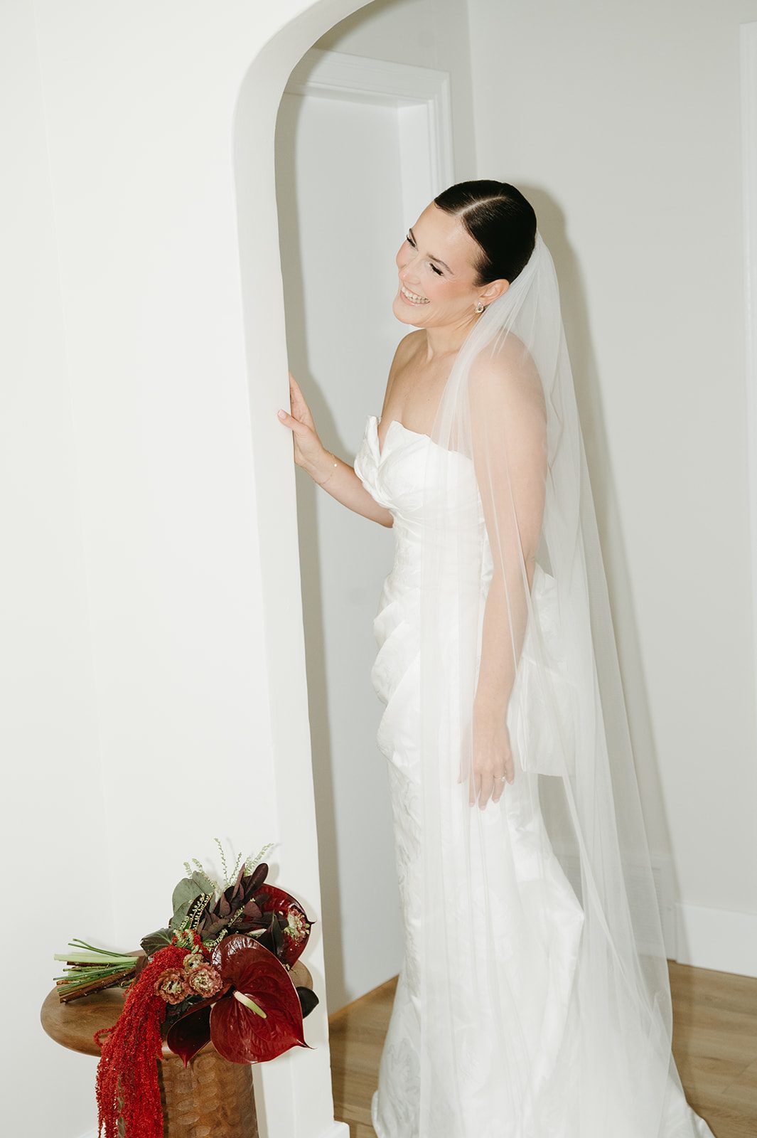 Andi + Logan Smiling bride in a modern white gown beside her burgundy sculptural wedding bouquet with cascading amaranthus.