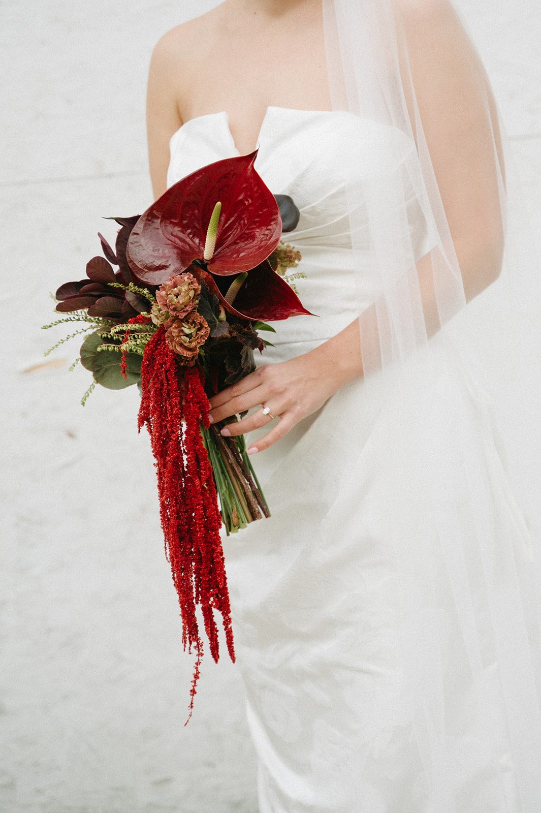 Andi + Logan Close up of sculptural wedding flowers with oversized burgundy anthurium, textural blooms, dark foliage and cascading red amaranthus.